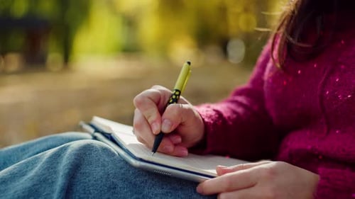 Closeup of a Woman's Hand Writing with a Pen in a Notebook in an Autumn Park