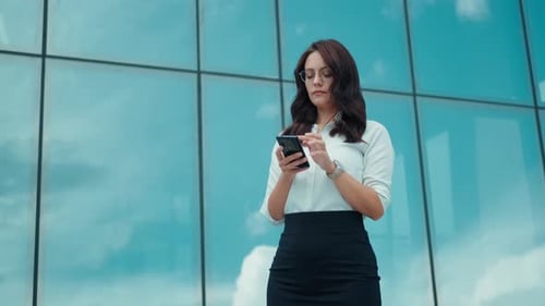 Portrait of a Business Woman Near a Modern Business Center Young Woman Uses a Smartphone Outdoors