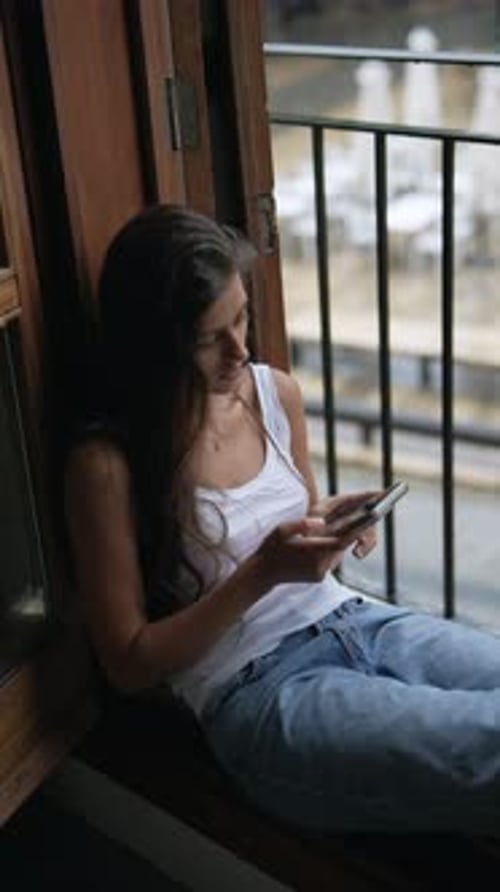 Woman using Cell Phone on Window Ledge