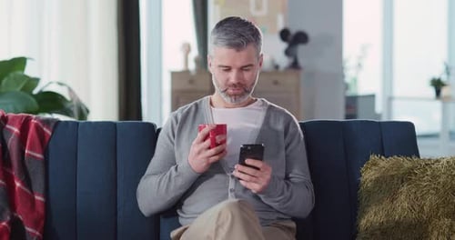 Man Relaxing on Couch Drinking Coffee and Using Phone