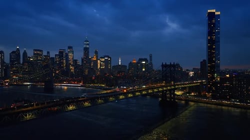 Impressive sight of night New York from the side of the river. Numerous cars ride by the bridges.