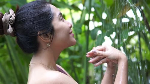 Side view footage of Asian woman smiling and taking bath in an outdoor shower room