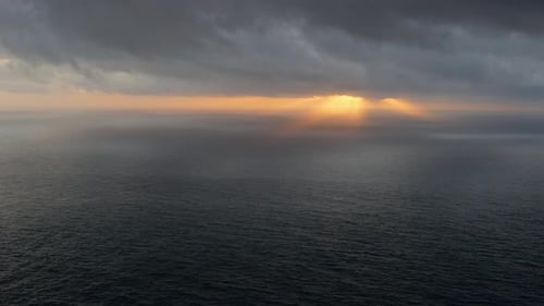 Sonnenuntergang über dem Meer mit dunklen Wolken darüber, Höhenblick