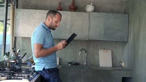 Man Using Tablet in Kitchen Next to Stove