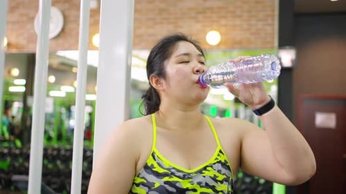 4K Plus size Asian woman drinking water after workout exercise at gym.