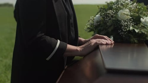 Hand Resting on Coffin at Outdoor Funeral