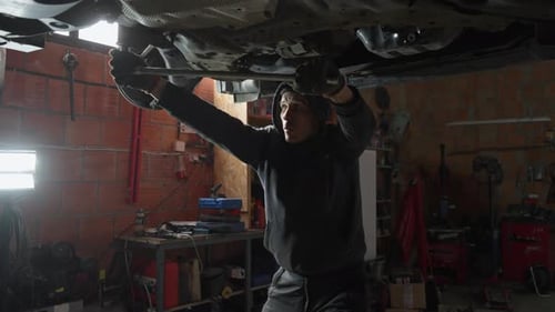 Mecânico de automóveis forte soltando um parafuso preso com uma chave longa em um veículo
