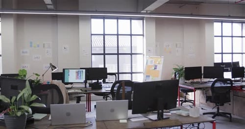 Office workspace with large windows, chairs and desks with computers, lamps and plants, slow motion