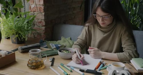 Carefree Young Woman Drawing Picture and Smiling Relaxing in Cozy Cafe Alone