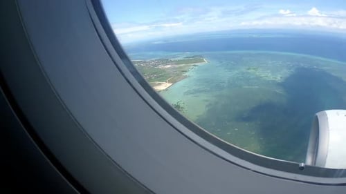 Airplane window view of the plane approaching the island revealing a coral reef, a small city, rooft