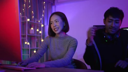 Young Woman Using Computer with Man Putting on Headphones