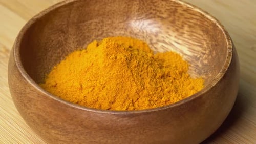 Turmeric Powder spice lies in wooden bowl and rotating on wooden board. Dry seasoning in spoon