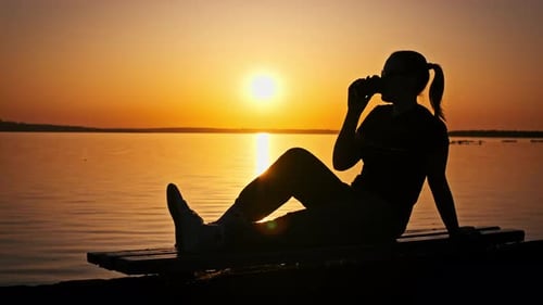 Woman Silhouette Drinks at Lakeside During Sunrise