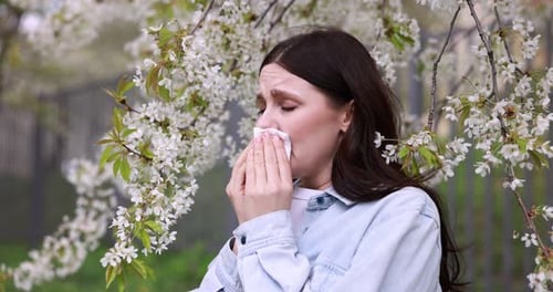 Seasonal allergy. Woman sneezing in park on spring day