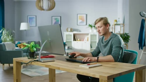 Porträt des konzentrierten jungen Mannes, der an einem PC arbeitet, während er an seinem Schreibtisch sitzt. In der