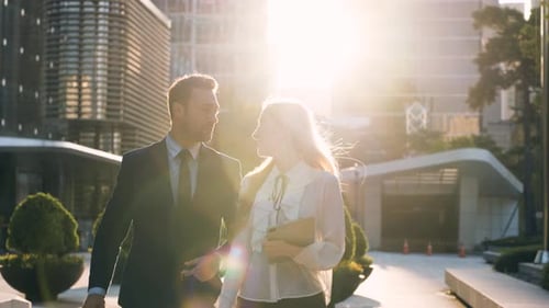 Smiling businessman and business woman talking on the go in setting sun sunlight, slow motion