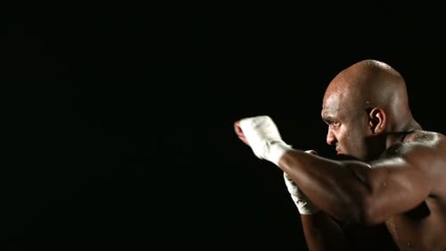 Intense man practices boxing punches in dark studio