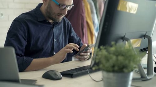 Man Uses Phone at Desk with Computer