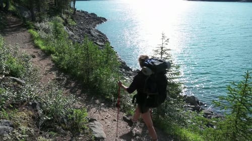 Mid adult woman hiking tranquil lakeside trail on sunny summer vacation day