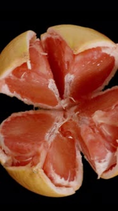 Vertical video. Cyclic Rotation of a Broken into Pieces Grapefruit, Isolated on a Black Background.