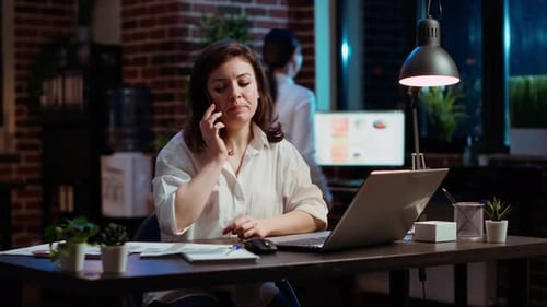 Woman Answering Phone Call While Working in Office at Computer Desk