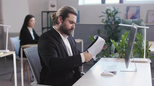 Professional Man Reviews Business Reports at Office Desk
