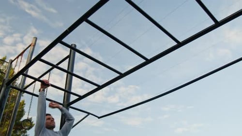 Young Man Going Across Monkey Bars in Outdoor Training area