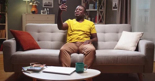 Man Video Calling on Phone, Sitting on Sofa