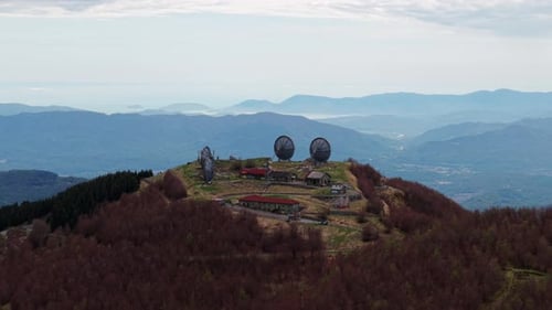 Aerial view of abandoned radar station on mountaintop surrounded by forested hills
