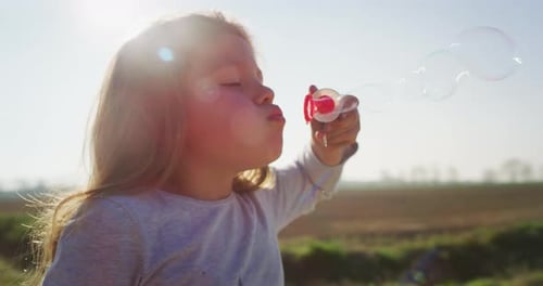 Authentic shot of little girl blowing soap bubbles in spring park on a sunny day.