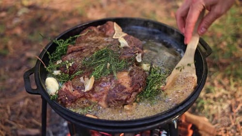 Campfire Cooking Sizzling Steak with Herbs and Garlic in a Cast Iron Skillet