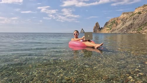 Woman Freelancer Works on Laptop Swimming in Sea on Pink Inflatable Ring Happy Tourist in Sunglasses