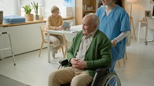 Caregiver Pushing Senior Man with Disability in Wheelchair to Another Senior