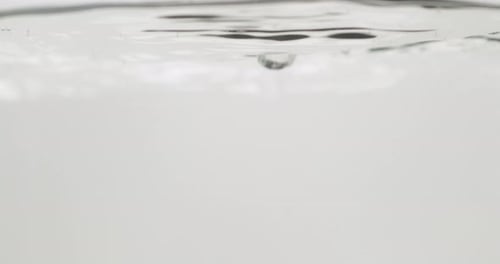 Wassertropfen, die auf eine ruhige Oberfläche fallen, isoliert auf reinweißer Farbe, Nahaufnahme