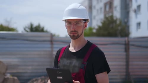Close Up Shot of Professional Construction Worker Wearing Hard Hat and Safety Glasses Holds Tablet