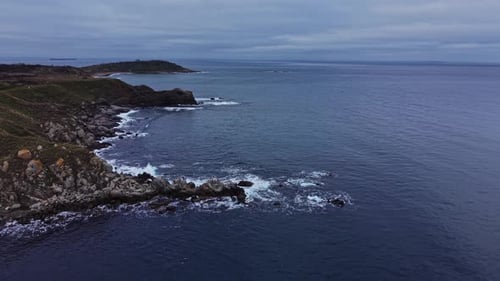 Waves crash on rocky shore near coast with distant land in view