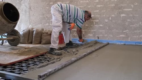 Construction worker spreading concrete above the radiant underfloor system.