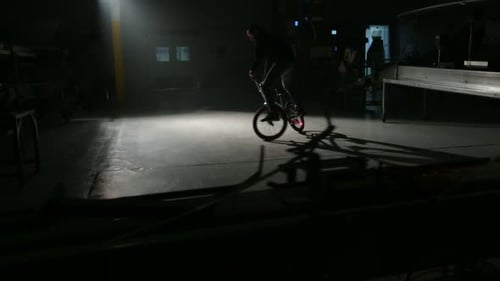 Bmx rider performing freestyle tricks in dark urban warehouse interior