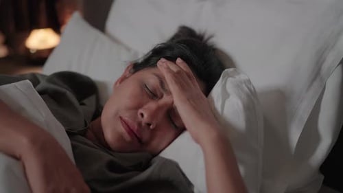 Woman Lying in Bed with Hand on Forehead