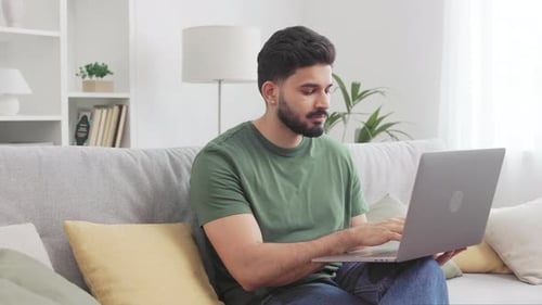 Homme hindou de bonne humeur travaillant sur un ordinateur portable dans une maison confortable