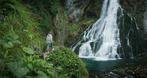 Girl admires the beauty of nature with her hands up. Woman enjoys view of powerful waterfall in the