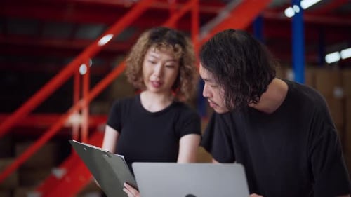 Two warehouse colleagues discuss work while using a laptop