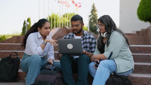 Happy Indian Student Using Laptop While Studying with Female Friends in Front of University Building