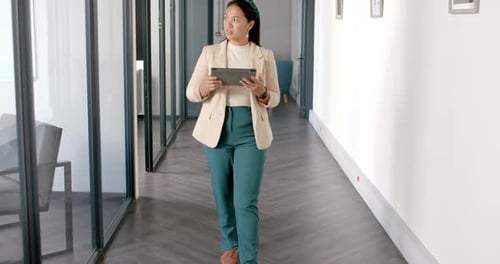 Walking in office hallway, woman holding tablet and smiling confidently