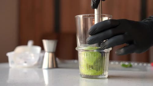 Hands Mashing Kiwi Fruit with Muddler in Glass