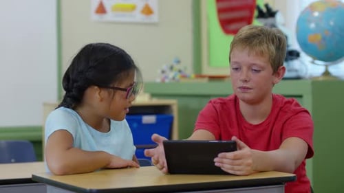 Two students collaborate using digital tablet technology in school classroom