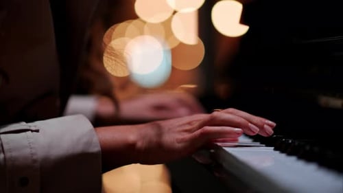 Close up of a woman's hands playing the piano with blurry lights on the background