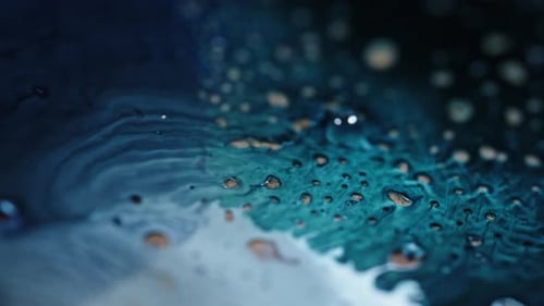 Blue and white liquids swirling and mixing together in a close-up shot with floating droplets