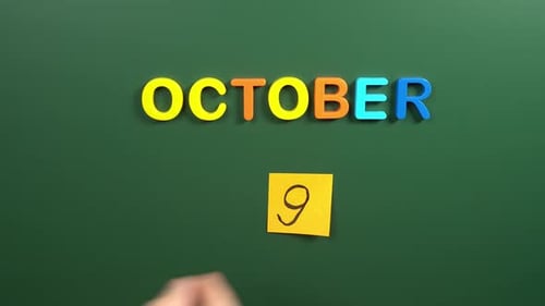 Hand sticking a sticker 9 October calendar day on school board. 9 date of October. Ninth day
