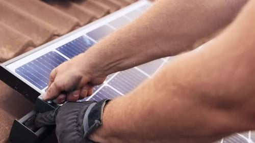 Closeup of PV professional hands installing Solar Panel on roof house, day
